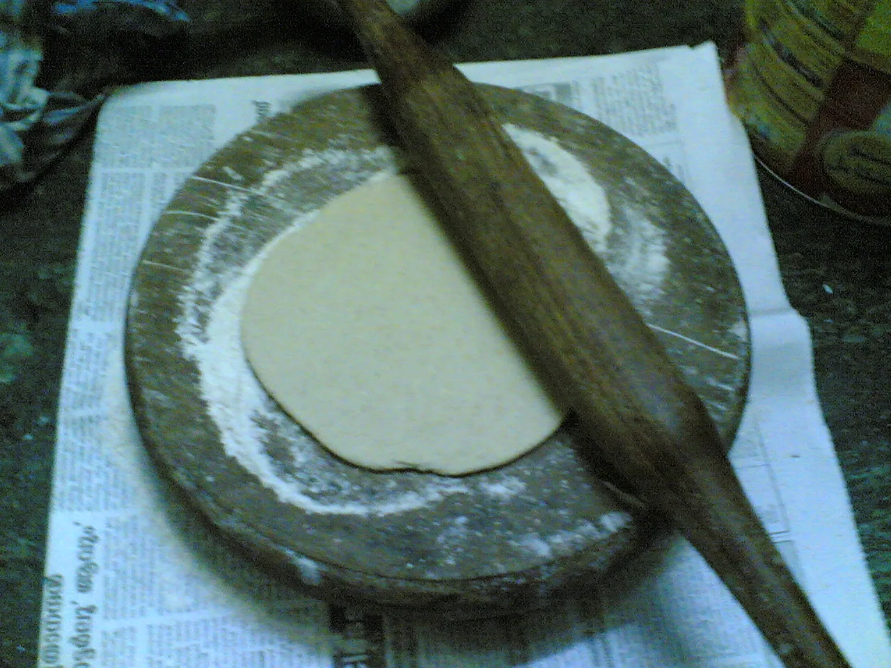 Dough rolled on a chakla — a Kerala kitchen, with a Malayalam newspaper underneath.