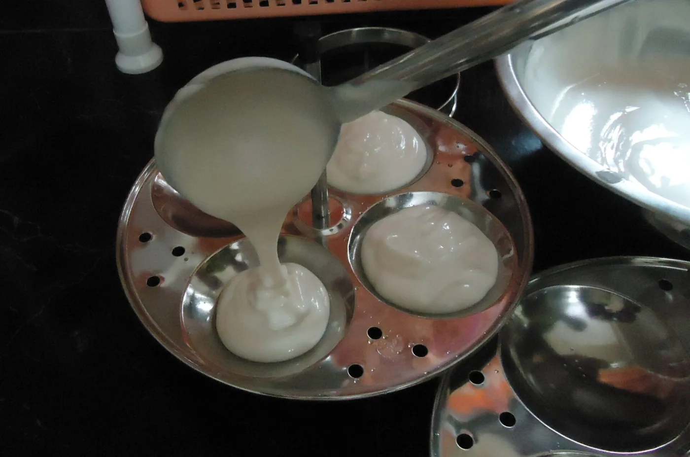 Batter ladled into a perforated idli tray.